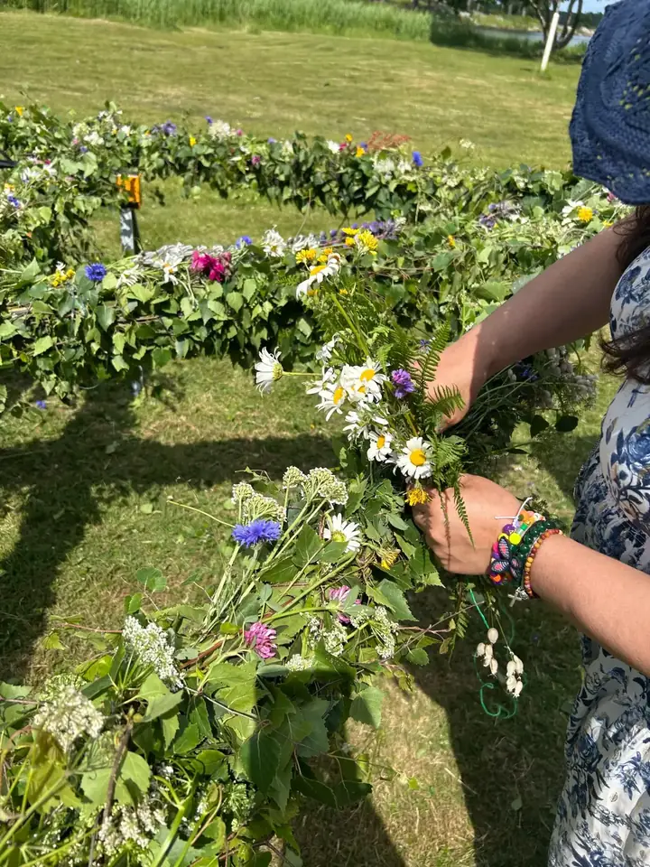 Panorama över festäng med folk, midsommarstång och gul byggnad