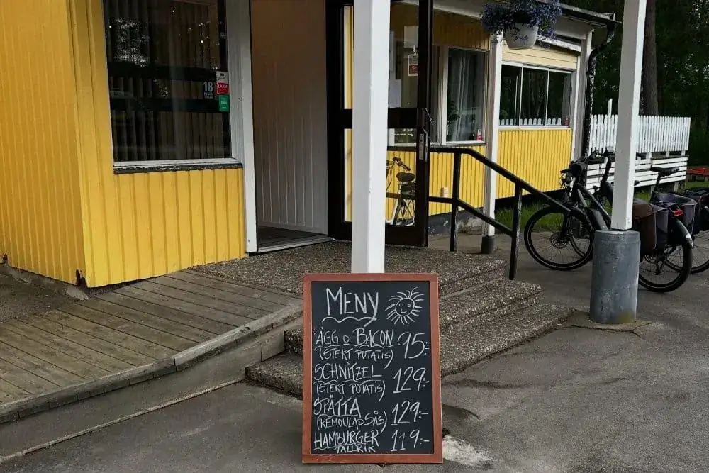 Menyskylt utanför gul bistrobyggnad med cyklar intill