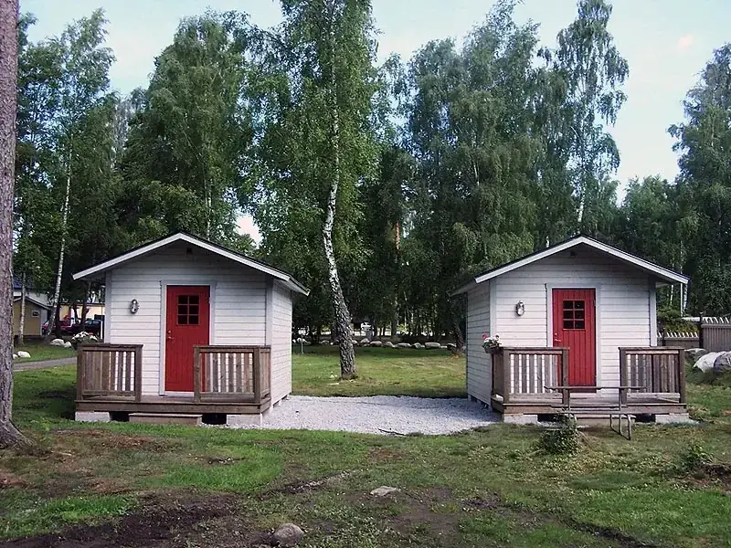 Två små vita stugor med röda dörrar bland björkar